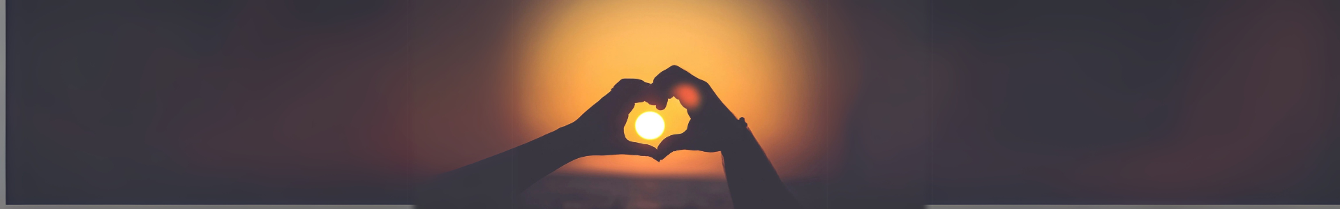 Two hands forming a heart shape against a glowing sunset, symbolizing love, unity, and emotional connection